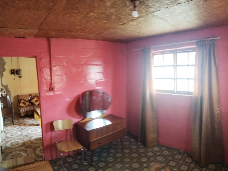 A bedroom featuring dated pink wall finishes, exposed particle board ceiling, and original grid-pattern floor tiles, requiring cosmetic updates and modernization.