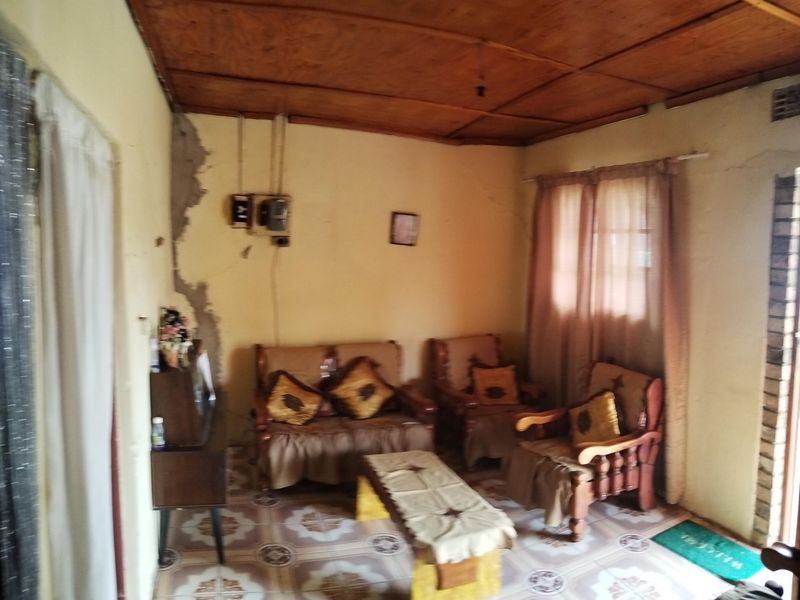 A living room featuring a wooden panel ceiling and tiled flooring, currently showing significant signs of wear and wall damage requiring maintenance.