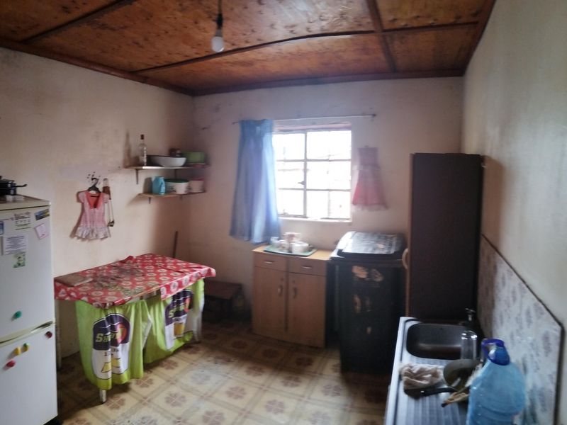A dated kitchen area featuring a wooden ceiling, tiled flooring, and basic sink installation, requiring significant cosmetic updates and modernization.