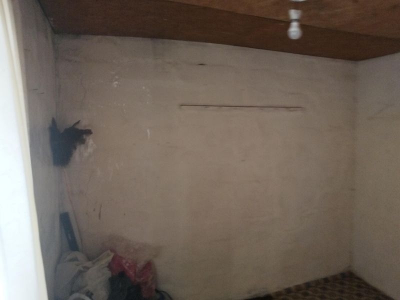 An empty bedroom space featuring an exposed wooden ceiling and requiring significant cosmetic renovation and wall repairs.