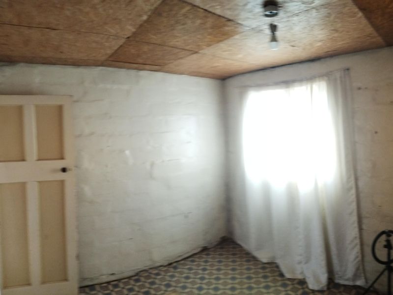 A vacant bedroom featuring painted brick walls, patterned vinyl flooring, and timber ceiling panels, requiring cosmetic updates to improve its overall condition.