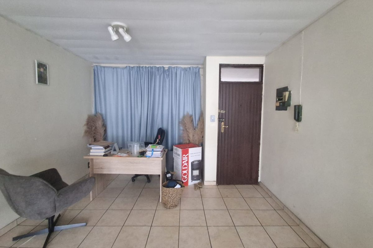 A functional living area featuring tiled flooring, a solid entrance door, and basic lighting fixtures, suitable for a home office or lounge space.