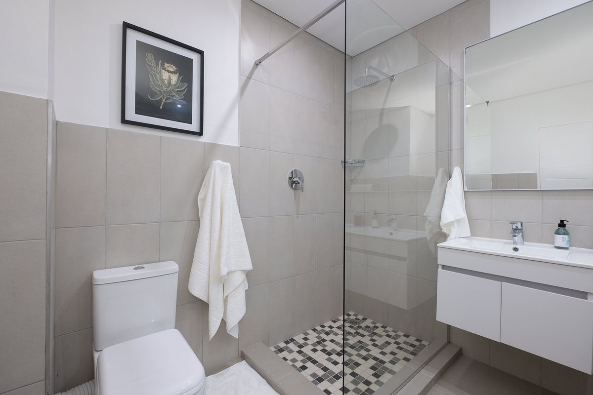 Modern bathroom featuring a glass-enclosed walk-in shower with mosaic tile flooring, a wall-mounted vanity with basin, and a contemporary toilet.