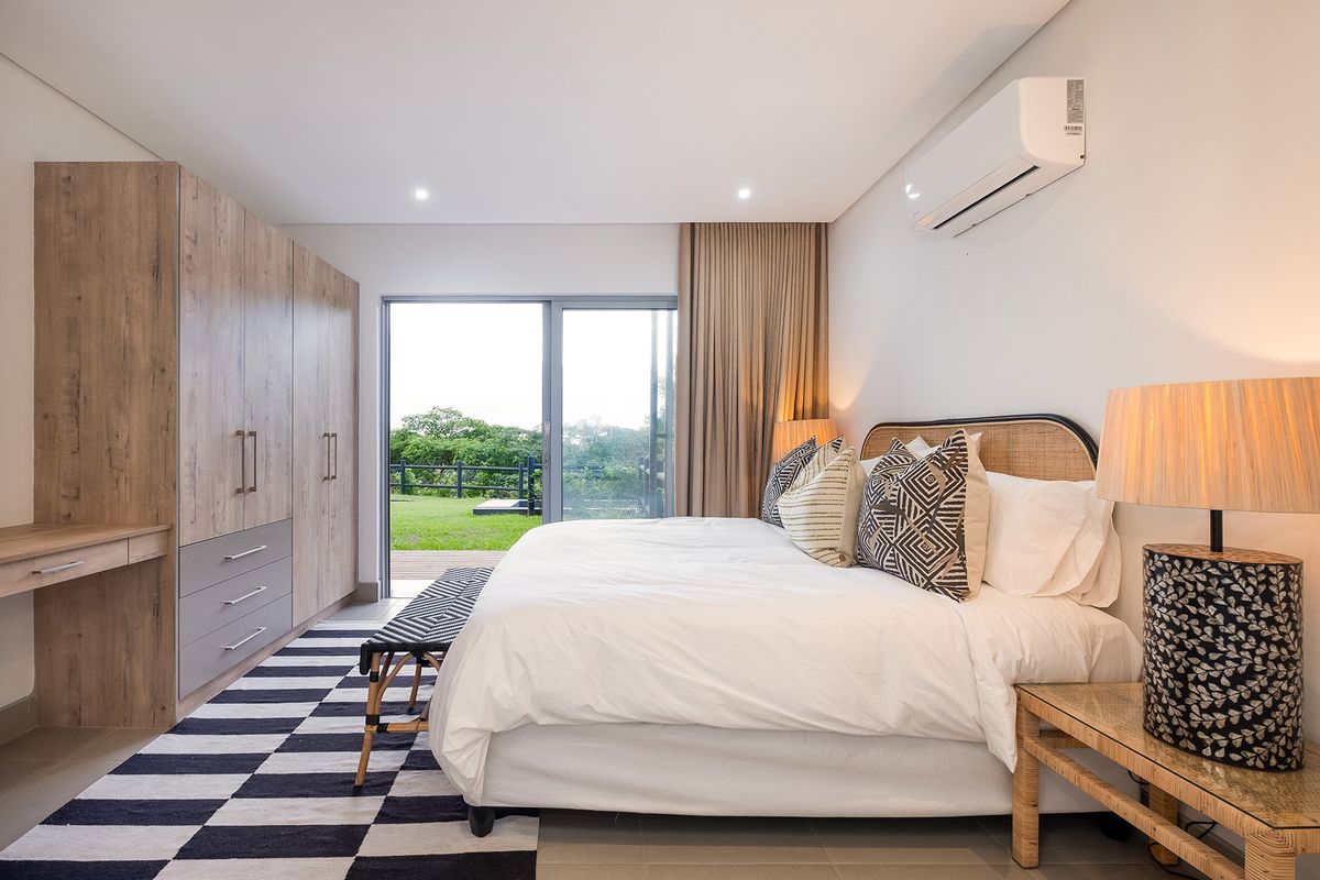 A modern bedroom featuring built-in wooden cabinetry, integrated desk space, and sliding glass doors leading to an outdoor patio area.