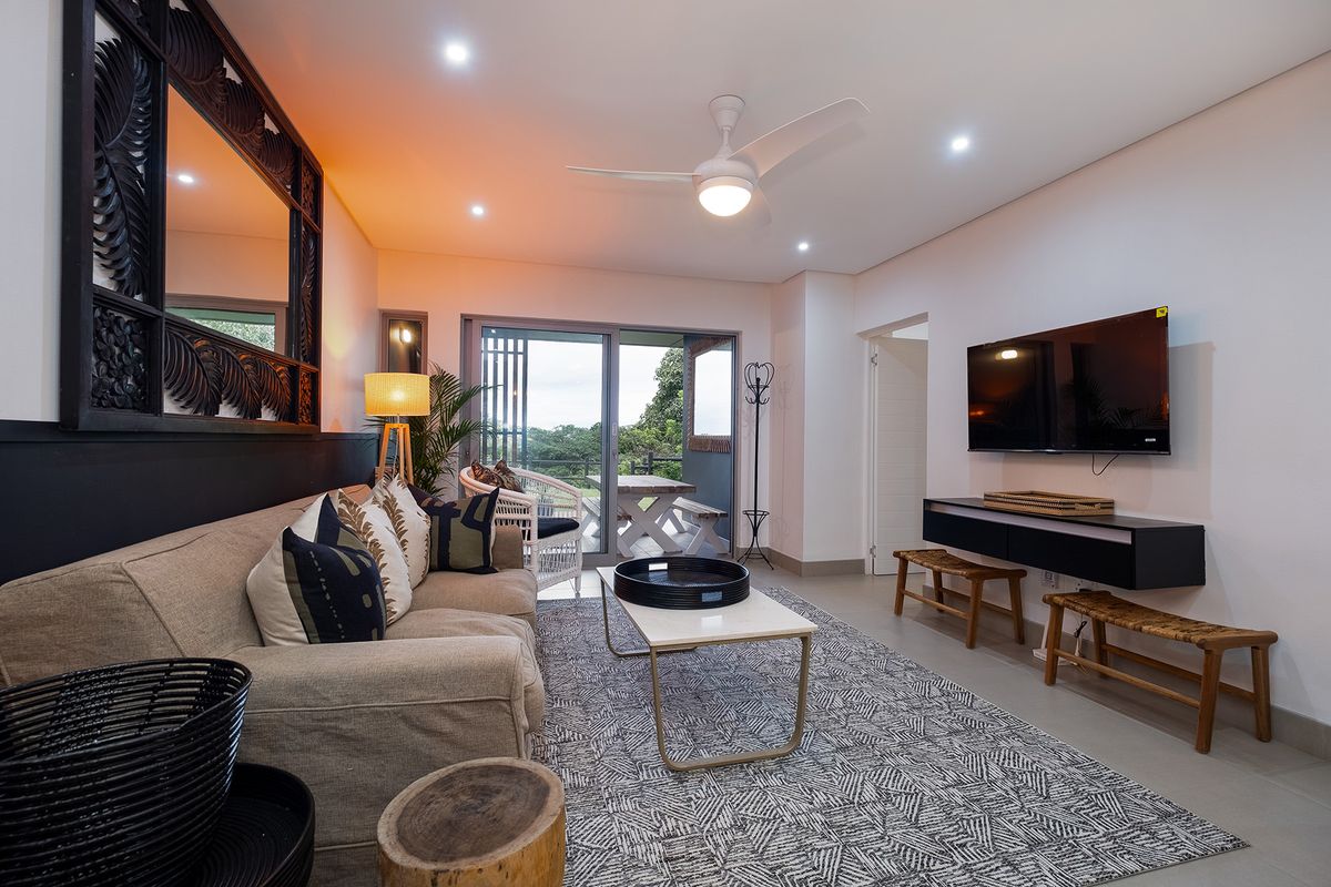 A well-lit living room featuring recessed ceiling lights, a modern ceiling fan, and sliding glass doors that open onto a private balcony.