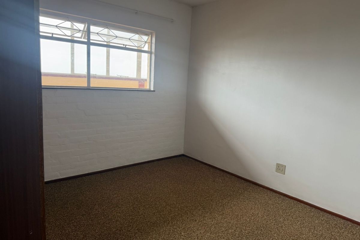 A vacant bedroom featuring neutral walls, carpeted flooring, and a single window providing natural light.