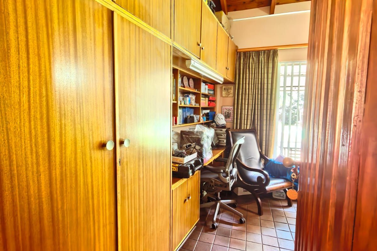 A functional study or bedroom featuring extensive built-in wooden cabinetry, tiled flooring, and a vaulted timber-paneled ceiling.