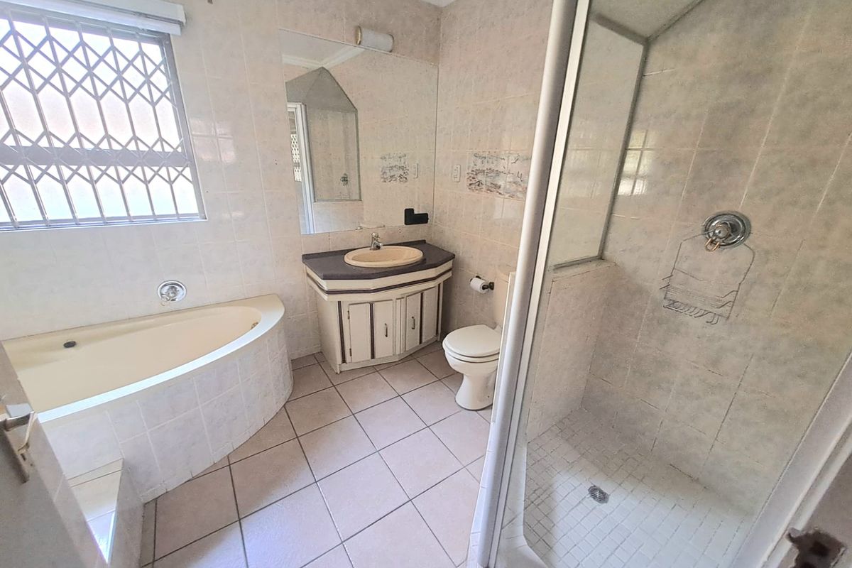 A functional bathroom featuring a corner bathtub, separate glass-enclosed shower, vanity basin, and toilet, finished with neutral wall and floor tiles.