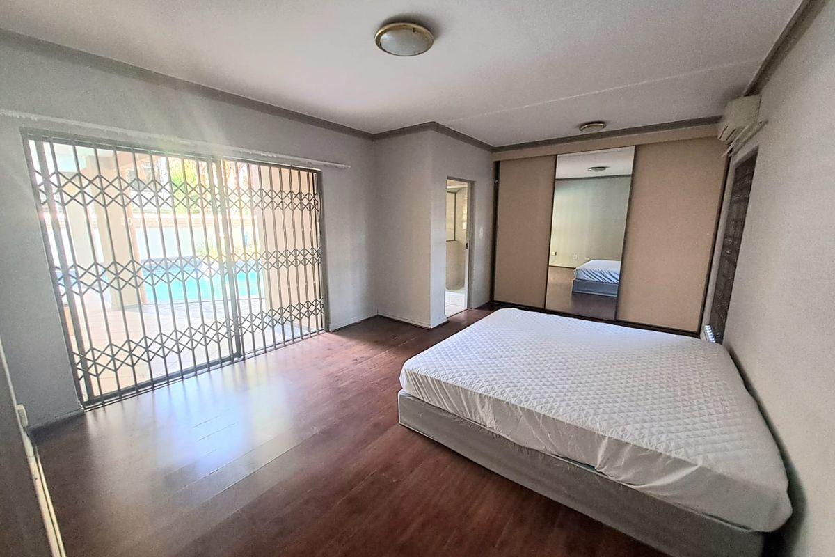 Spacious bedroom featuring built-in cupboards with mirrored doors, laminate flooring, and sliding security gate access to the outdoor pool area.