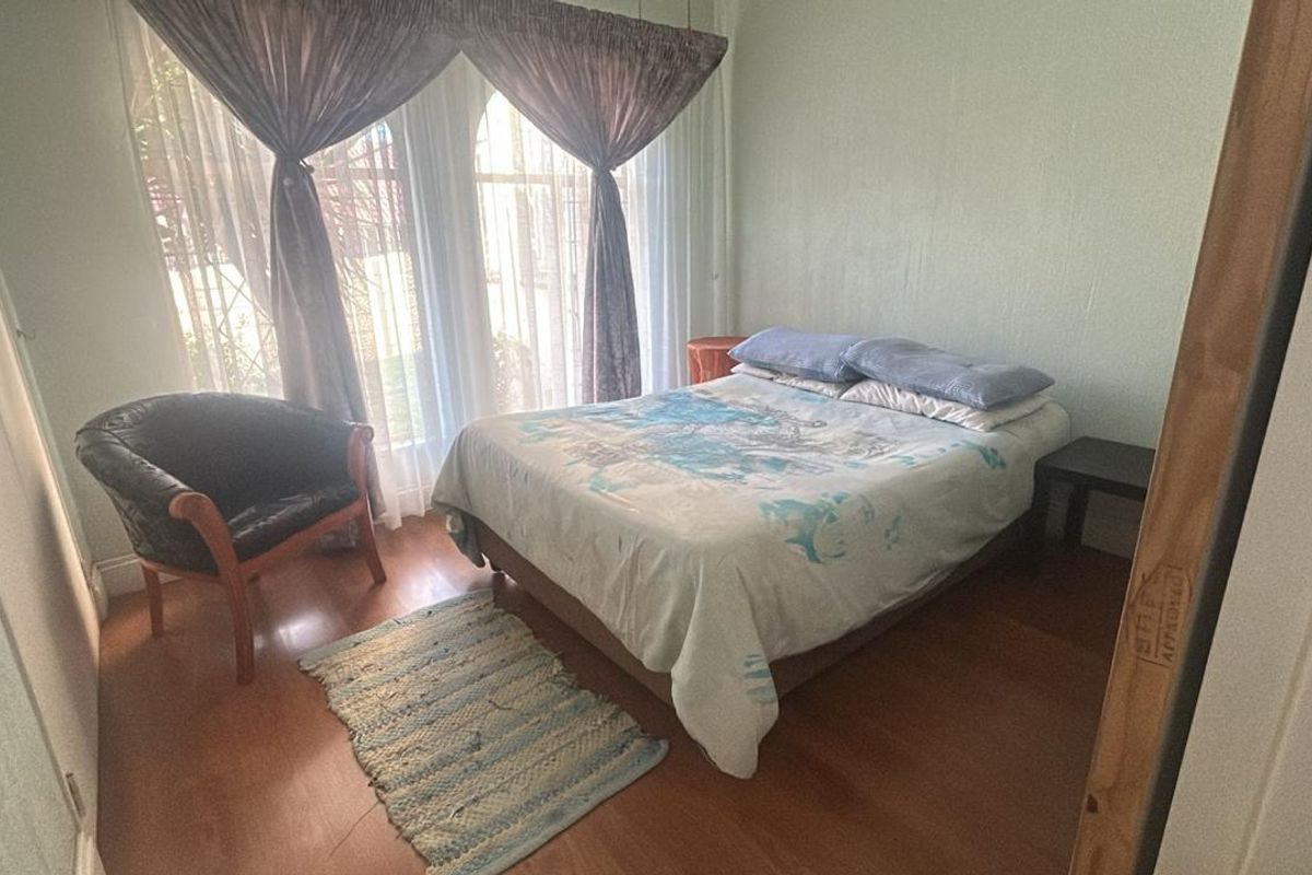A bedroom featuring laminate flooring and large windows with curtains, providing natural light.