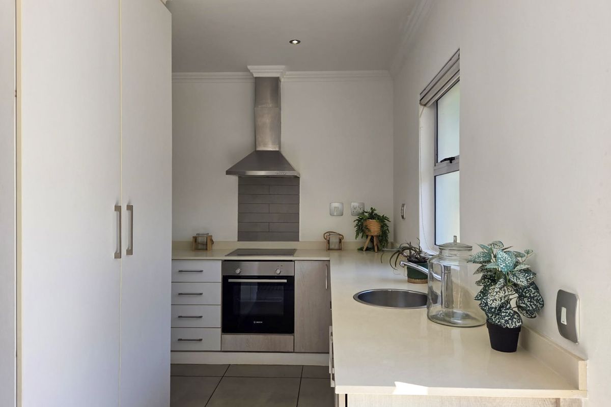 A compact, modern kitchen featuring built-in cabinetry, a stainless steel oven, hob, extractor fan, and a circular sink with stone-look countertops.