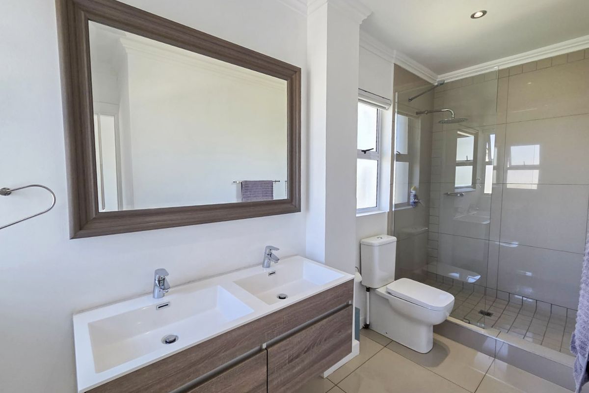 Modern bathroom featuring a double vanity with wood-finish cabinetry, a large framed mirror, a glass-enclosed walk-in shower, and tiled flooring.