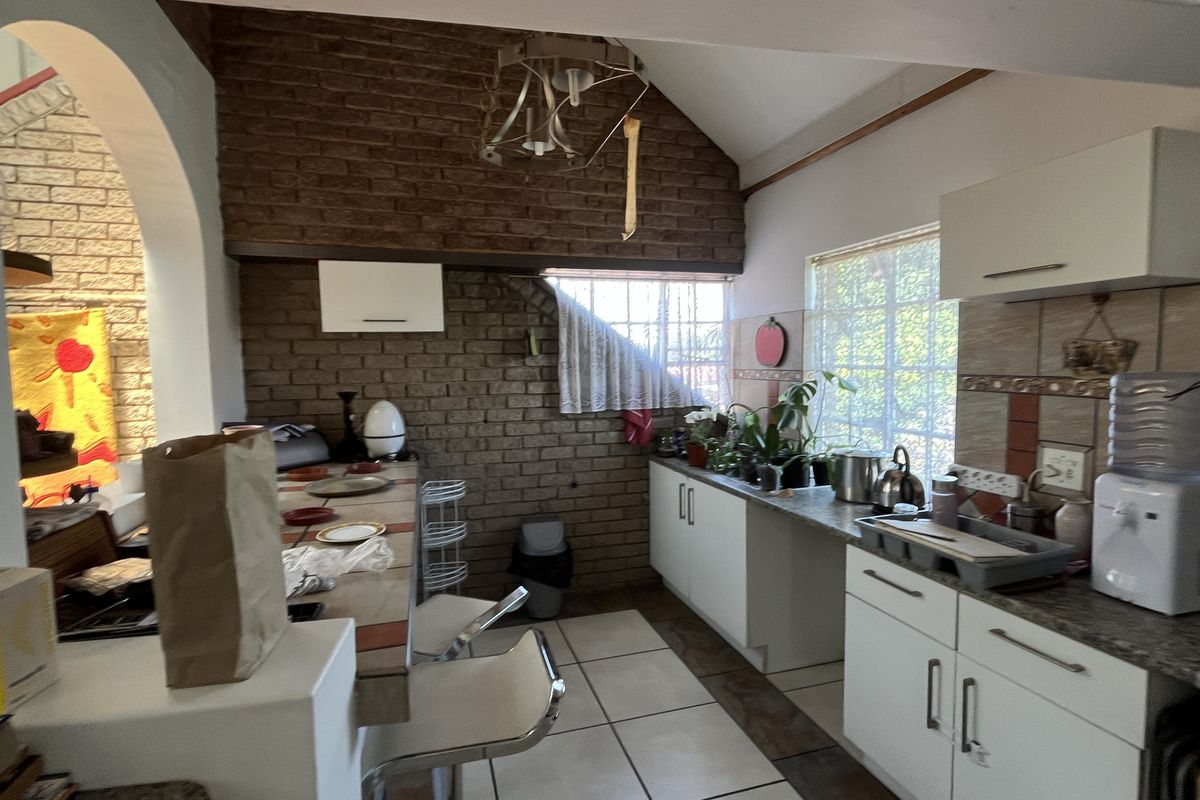 A rustic kitchen featuring exposed brick walls, white cabinetry, tiled countertops, and a breakfast bar area with vaulted ceilings.