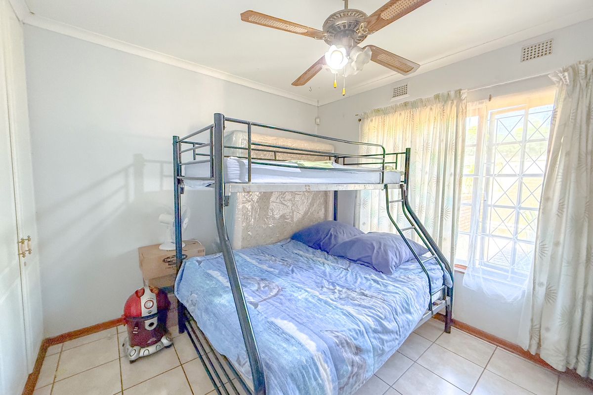 A bedroom featuring tiled flooring, a ceiling fan, and security bars on the window.