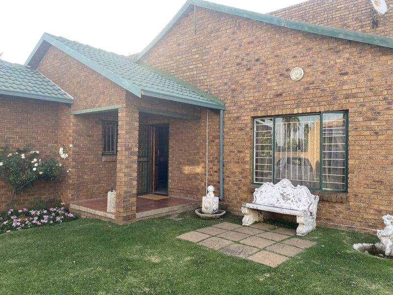 A view of the rear exterior featuring face-brick walls, a covered entrance porch, tiled patio area, and a small garden space.