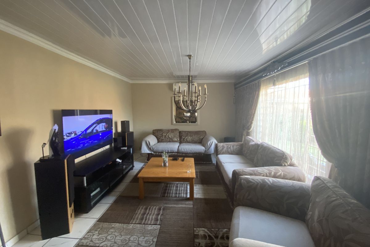 A comfortable living room featuring tiled flooring, a classic chandelier, and large windows with curtains, providing a functional and inviting space.