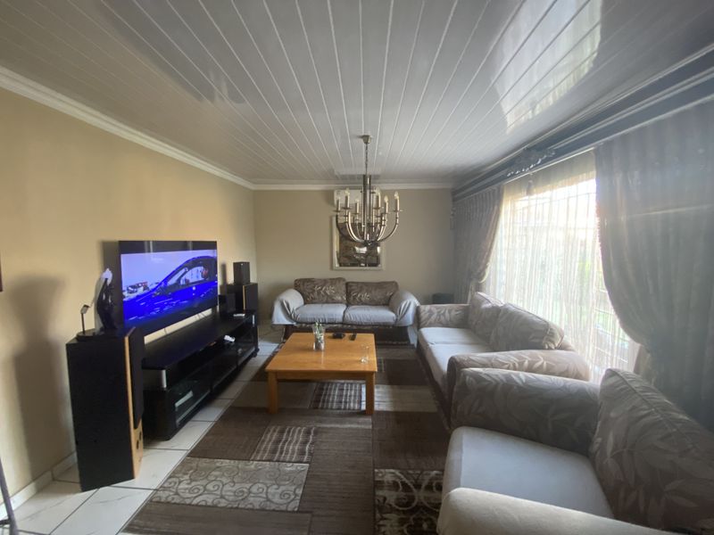 A comfortable living room featuring tiled flooring, a classic chandelier, and large windows with curtains, providing a functional and inviting space.