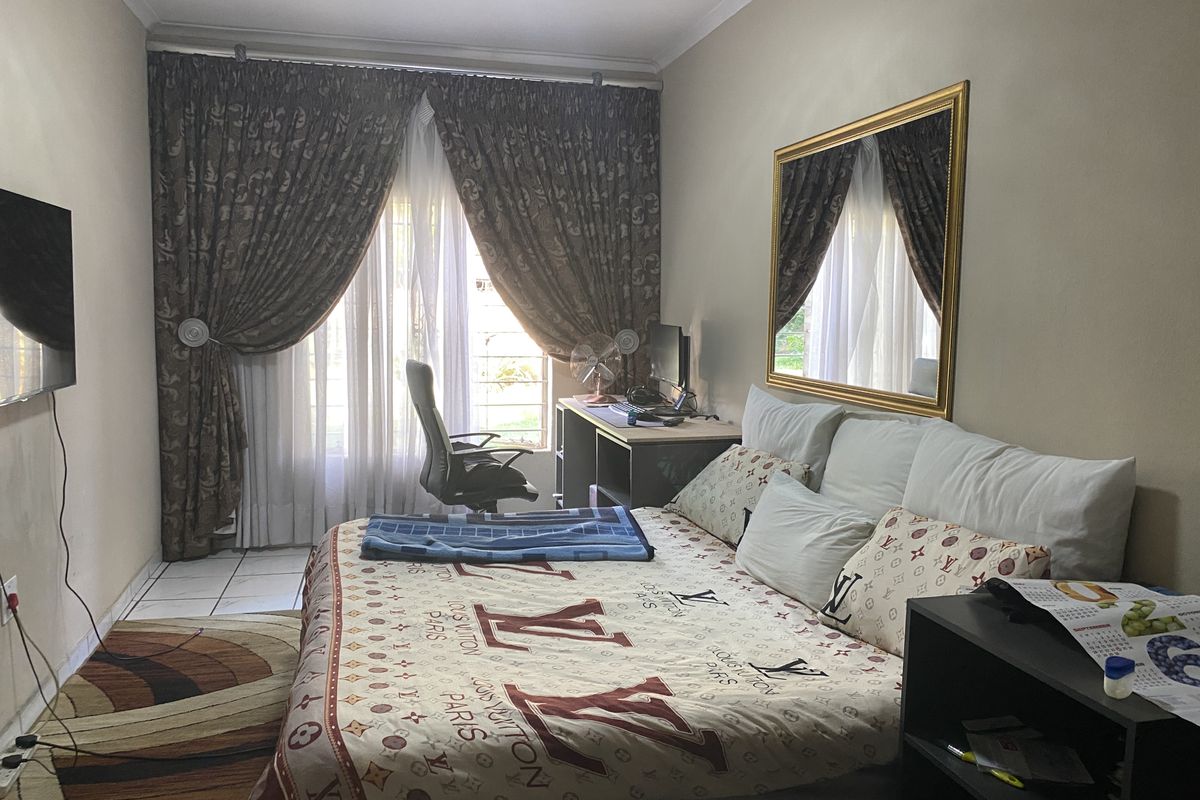 A functional bedroom featuring tiled flooring, a large window with curtain treatments, and a wall-mounted mirror.