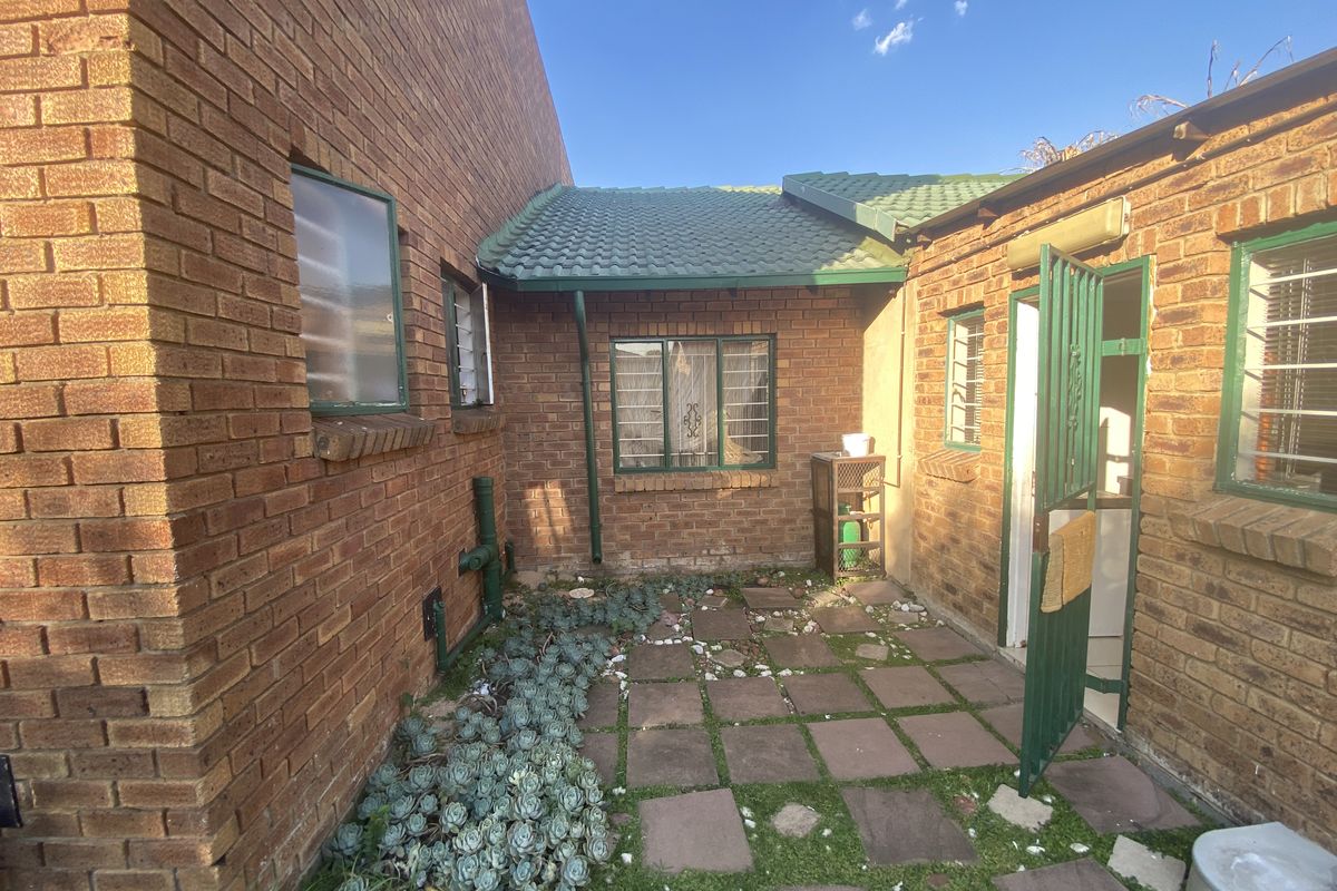A private rear courtyard area featuring brick walls, paved flooring, and green metal security gates, providing a functional outdoor space.