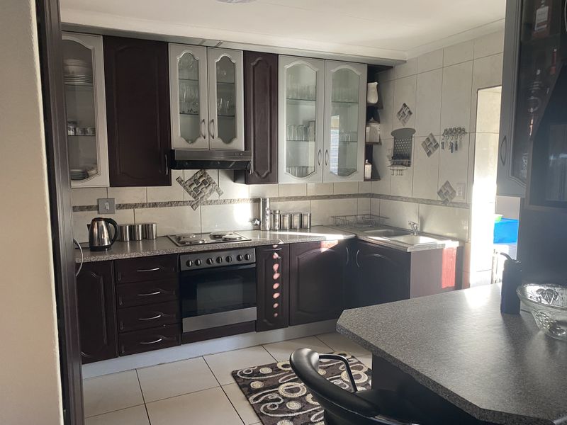 A functional kitchen featuring dark wood cabinetry, integrated oven and hob, tiled splashbacks, and a breakfast bar counter.