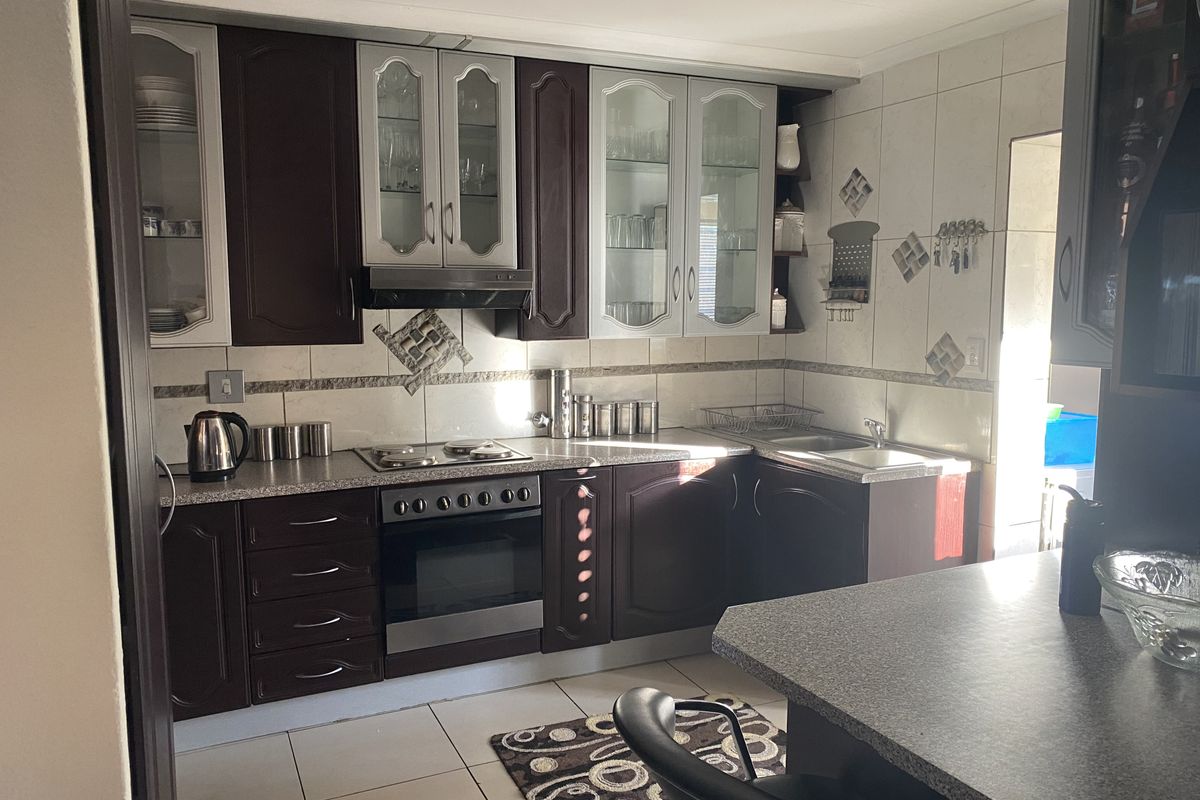 A functional kitchen featuring dark wood cabinetry, integrated oven and hob, tiled splashbacks, and a breakfast bar counter.