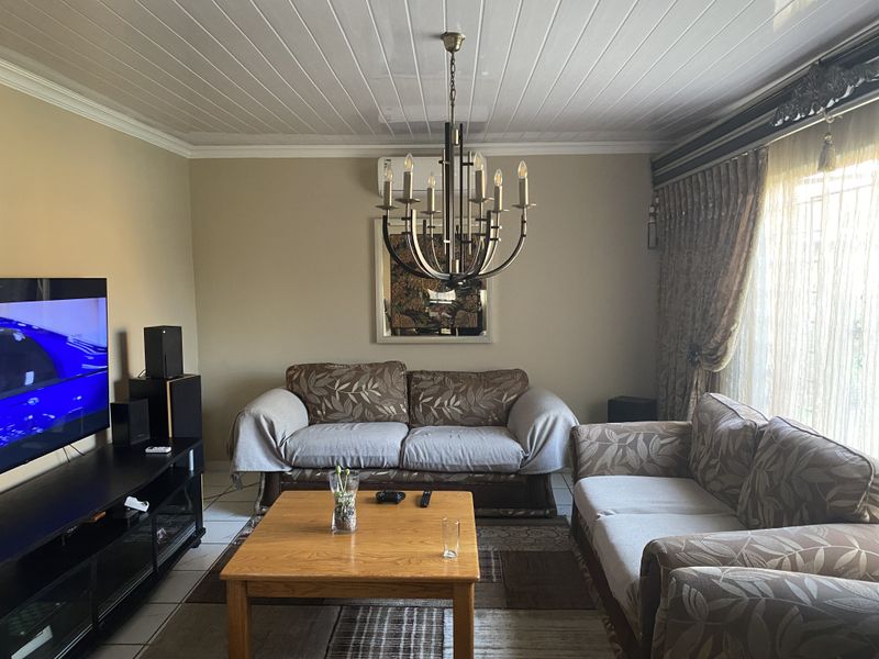 A comfortable living room featuring a decorative chandelier, tiled flooring, and a wall-mounted air conditioning unit.