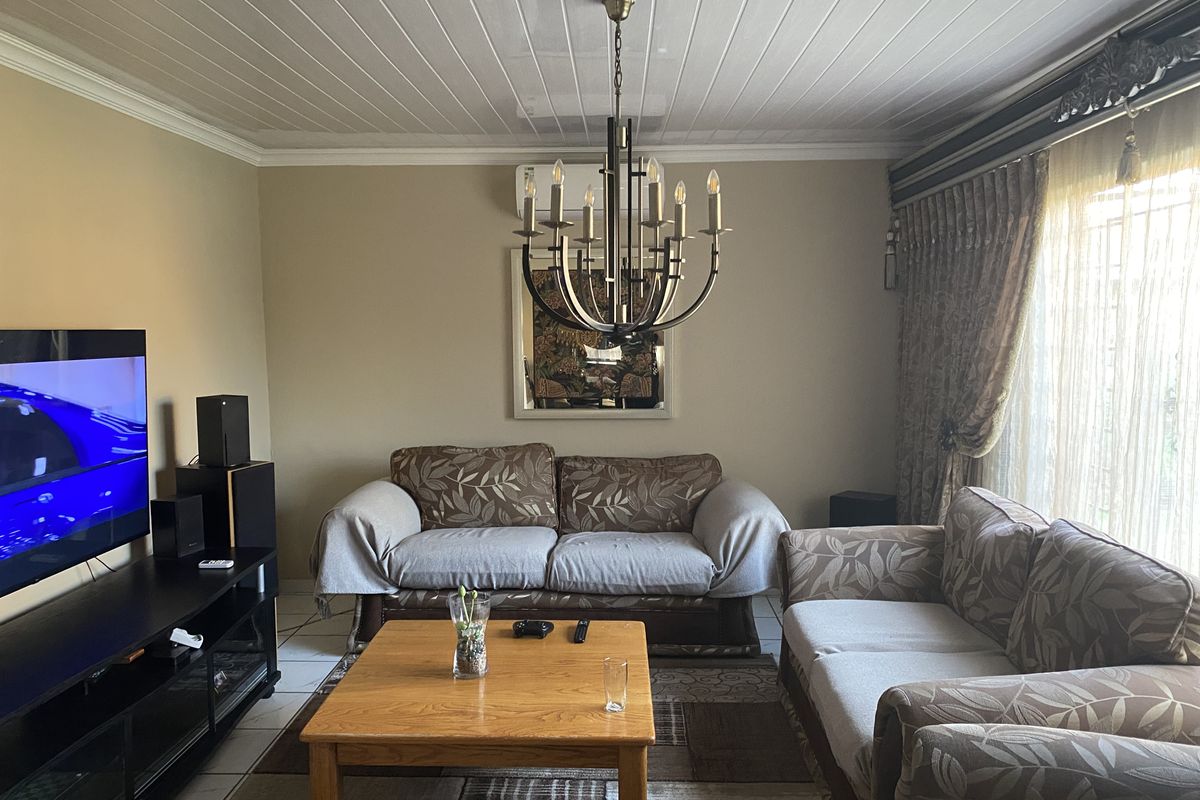A comfortable living room featuring a decorative chandelier, tiled flooring, and a wall-mounted air conditioning unit.
