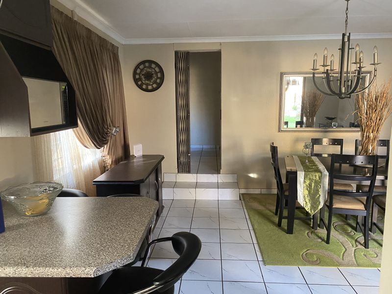 Open plan dining and kitchen area featuring tiled flooring, a breakfast counter, and a raised doorway leading to the hallway.