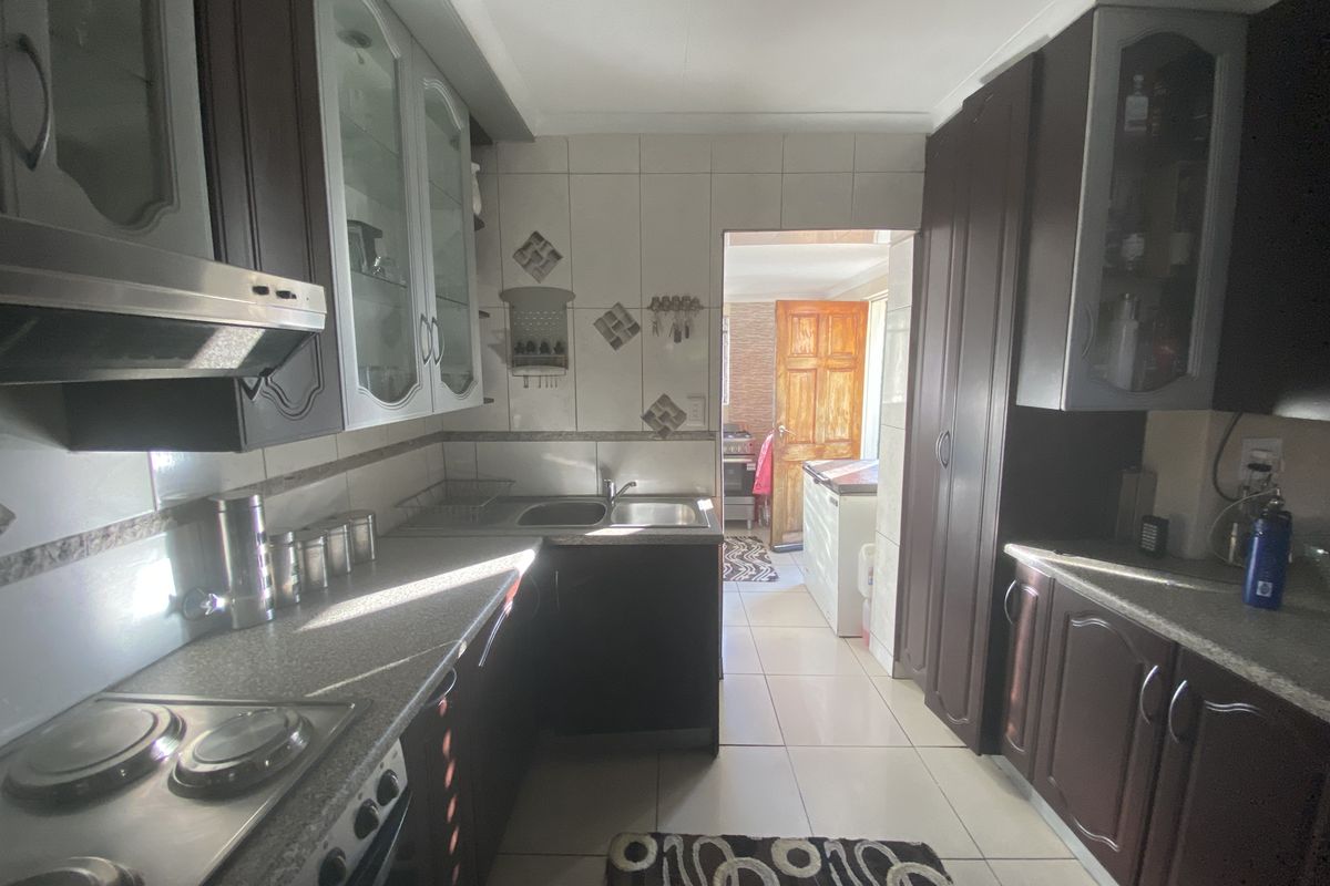 A functional kitchen featuring dark wood cabinetry, integrated stove and extractor fan, tiled flooring, and a convenient layout leading to an adjacent utility area.