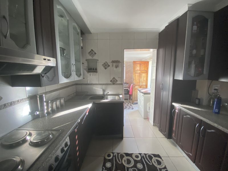 A functional kitchen featuring dark wood cabinetry, integrated stove and extractor fan, tiled flooring, and a convenient layout leading to an adjacent utility area.