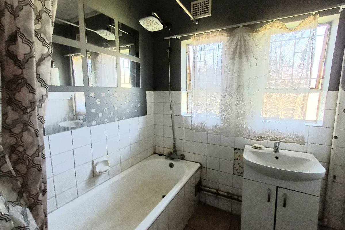 A dated bathroom featuring a bathtub with shower attachment, a vanity basin, and tiled wall finishes requiring maintenance and cosmetic updates.
