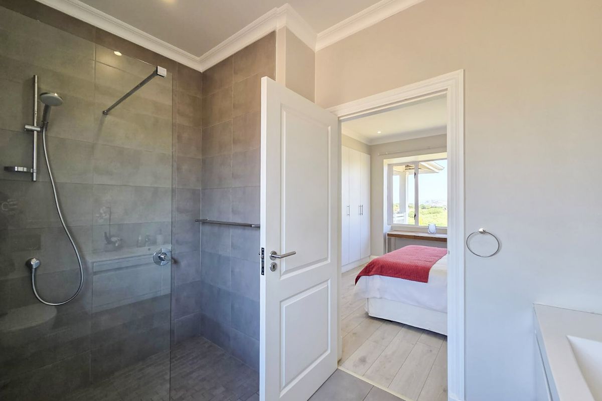 Modern bathroom featuring a walk-in glass shower with grey tiling, leading into a bright bedroom with built-in cabinetry.