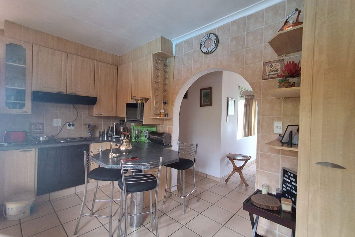 A functional kitchen featuring light wood cabinetry, tiled splashbacks, a breakfast bar, and an arched entryway leading to the adjacent living space.