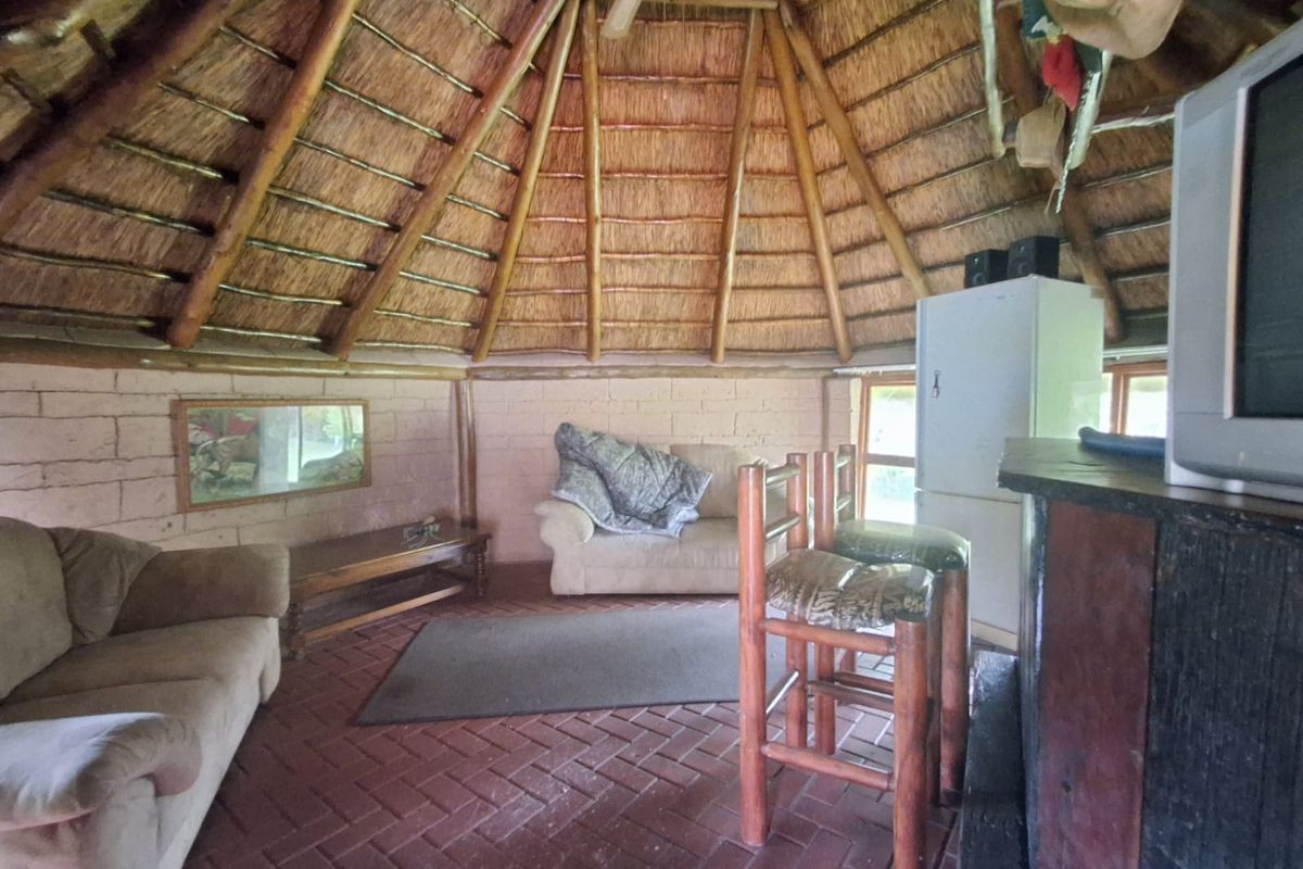 A rustic circular living area featuring a traditional thatched roof, exposed brick walls, and terracotta tiled flooring, creating a unique, dated interior space.