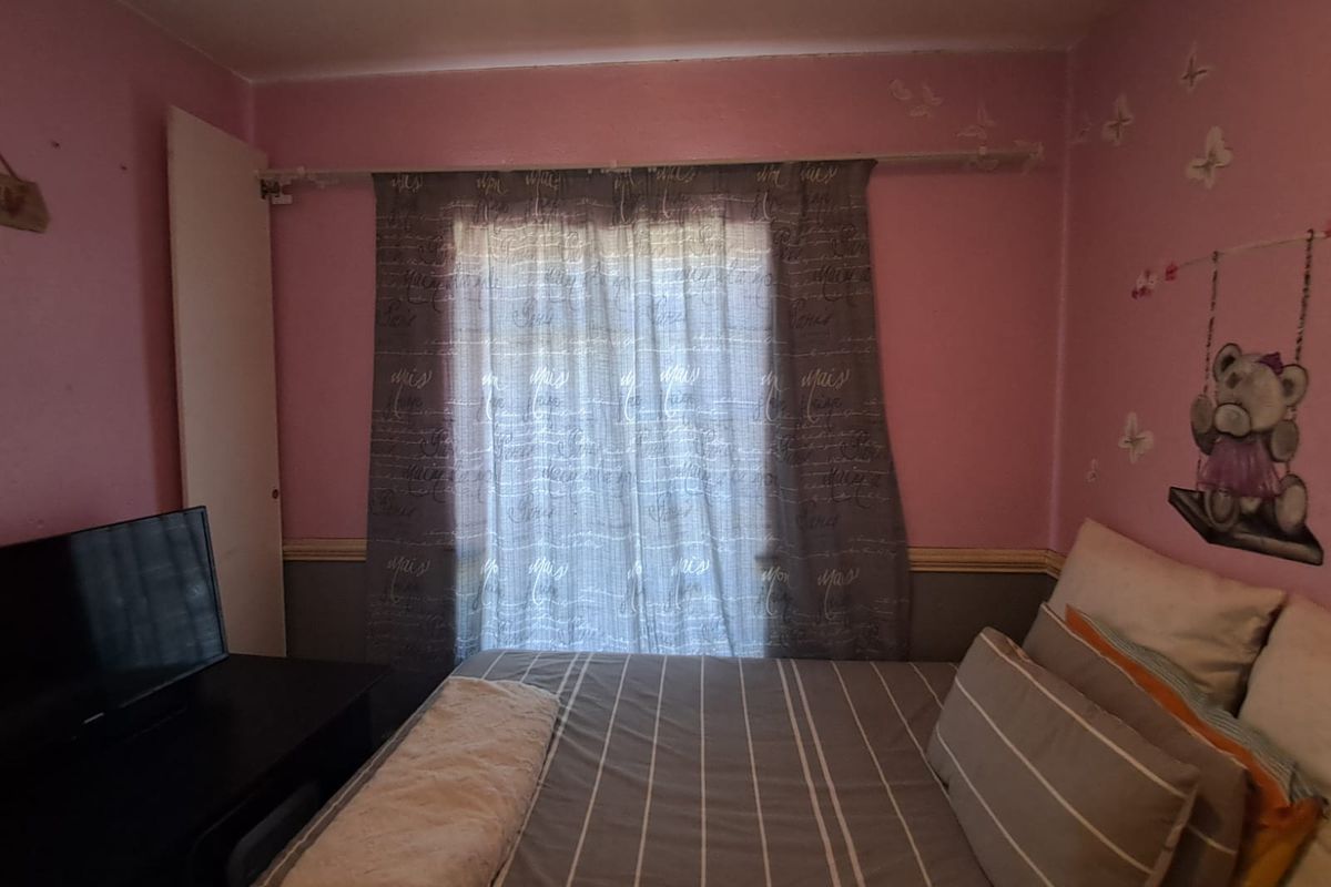 A bedroom featuring pink painted walls with a chair rail, window with curtain rod, and built-in closet door.