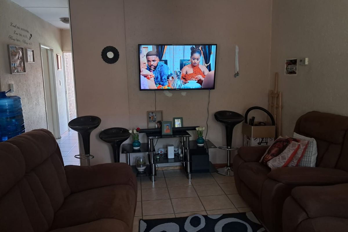 A living room area featuring tiled flooring and a wall-mounted television, providing a functional space for relaxation and entertainment.