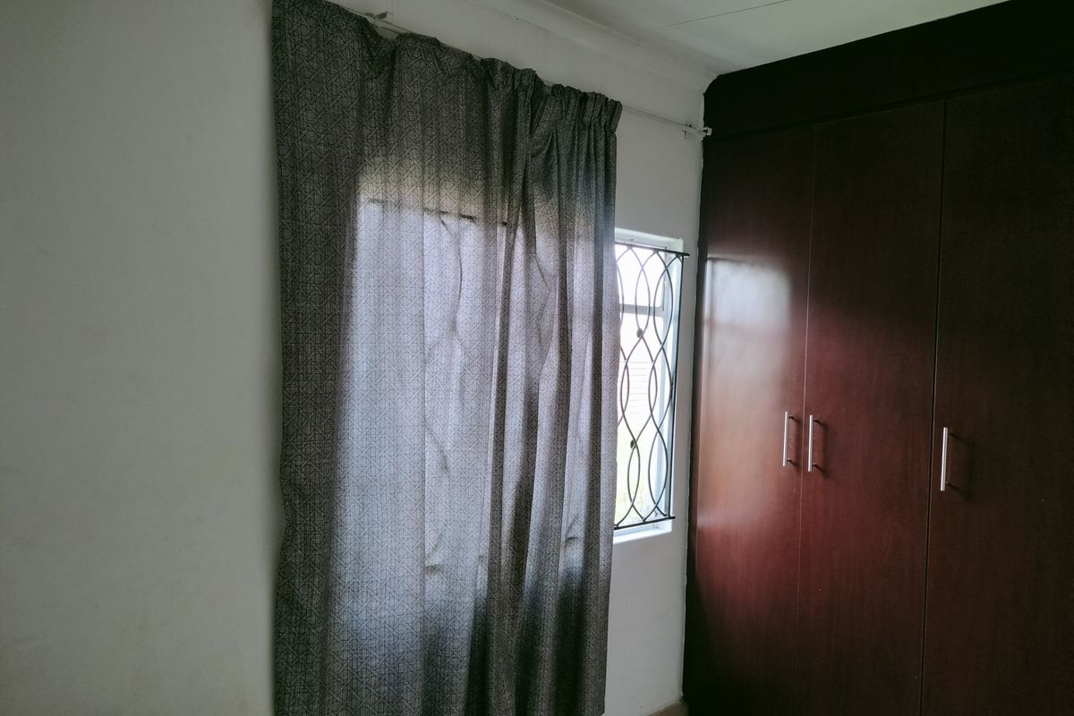 A bedroom featuring built-in dark wood cabinetry and a window with security bars.