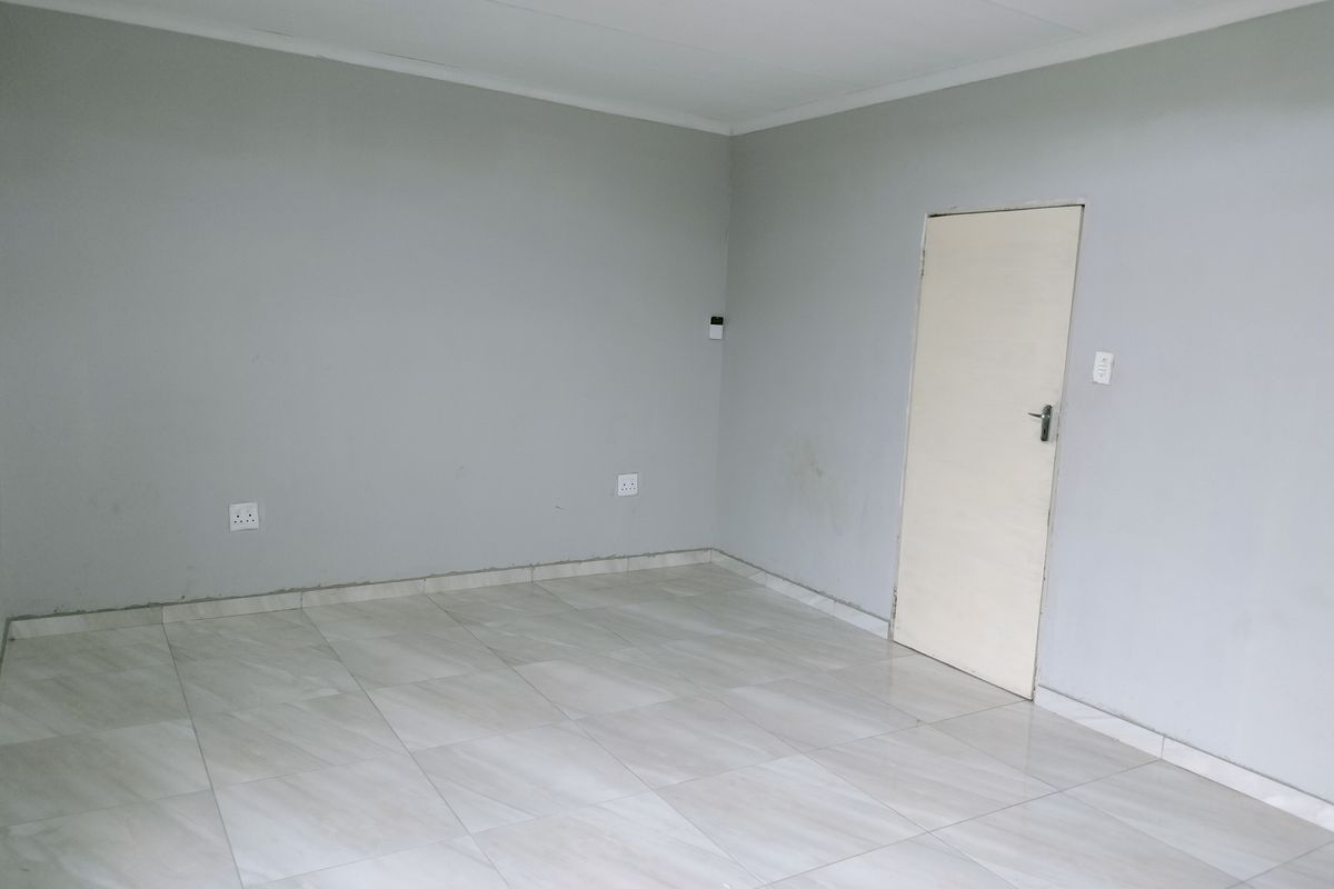 A clean, empty living room featuring neutral grey walls, tiled flooring, and a single interior door.