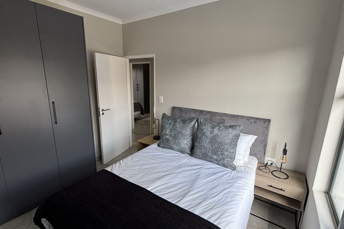 A well-maintained bedroom featuring built-in cupboards, neutral wall finishes, and large windows allowing for natural light.