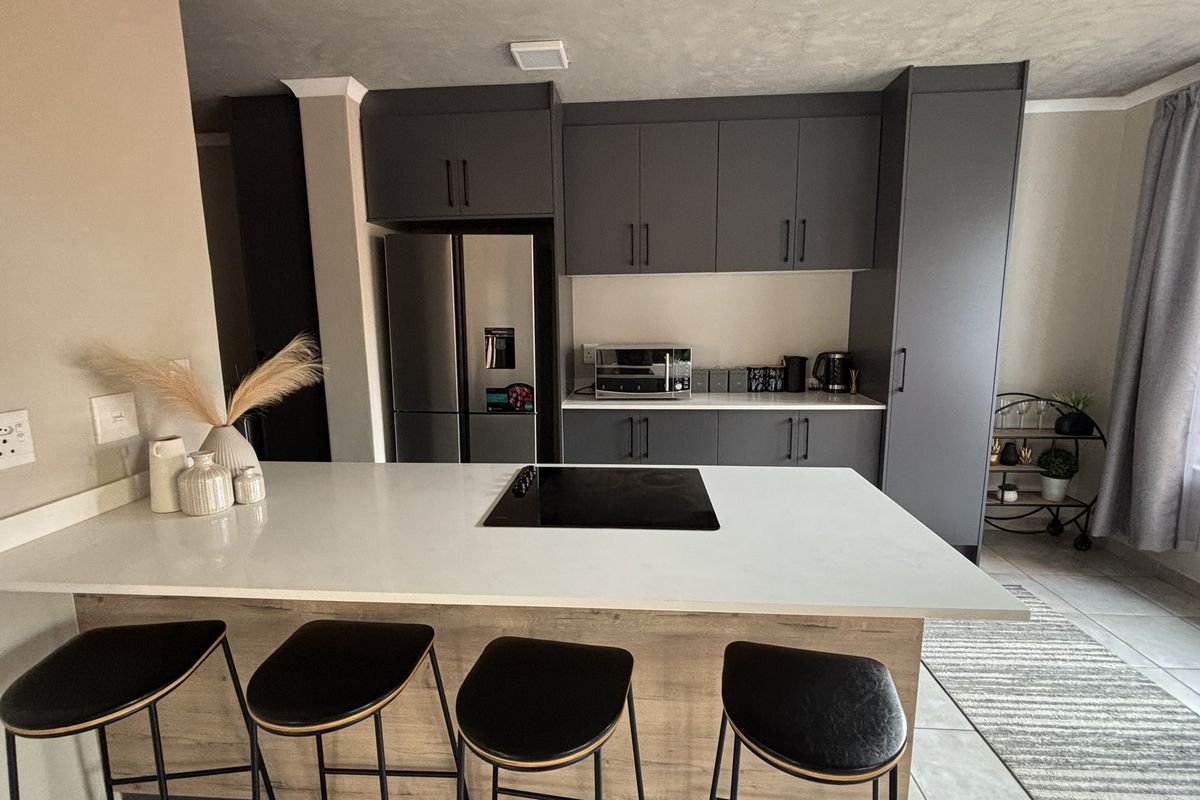 Modern open-plan kitchen featuring dark grey cabinetry, a white stone island countertop with an integrated electric hob, and tiled flooring.