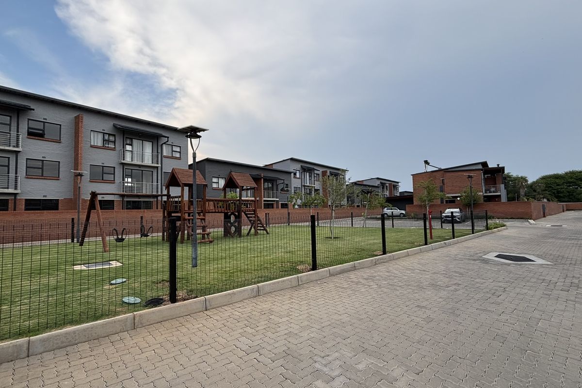 A view of the townhouse complex exterior featuring a communal lawn, playground area, and paved driveway access.