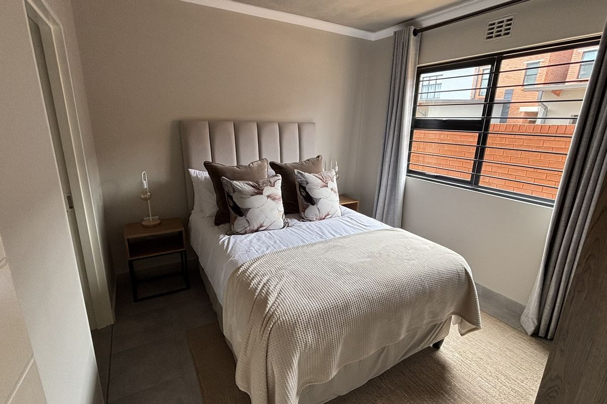 A well-maintained bedroom featuring neutral wall tones, tiled flooring, and a window with security bars, providing a comfortable and functional living space.