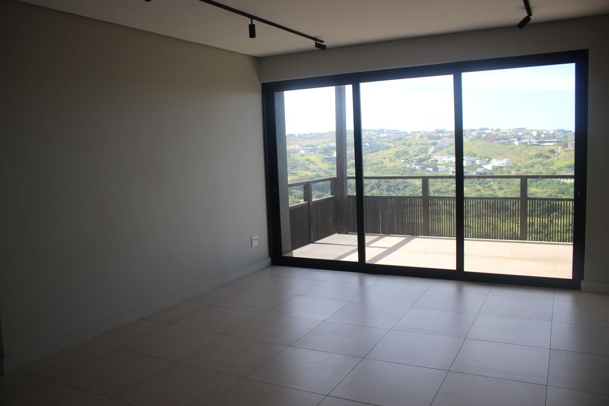An empty living area featuring large sliding glass doors that open onto a balcony with scenic landscape views and modern track lighting.
