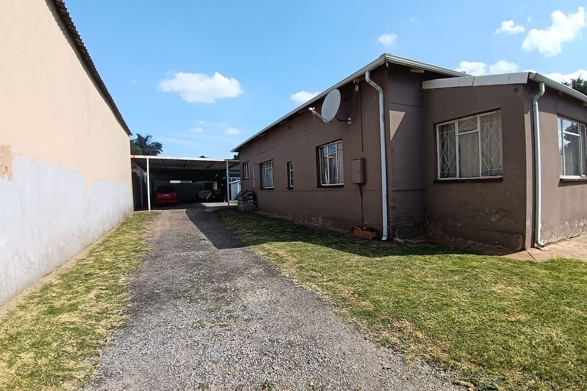 Rear view of the property featuring a gravel driveway, carport, and exterior wall with security bars on the windows.