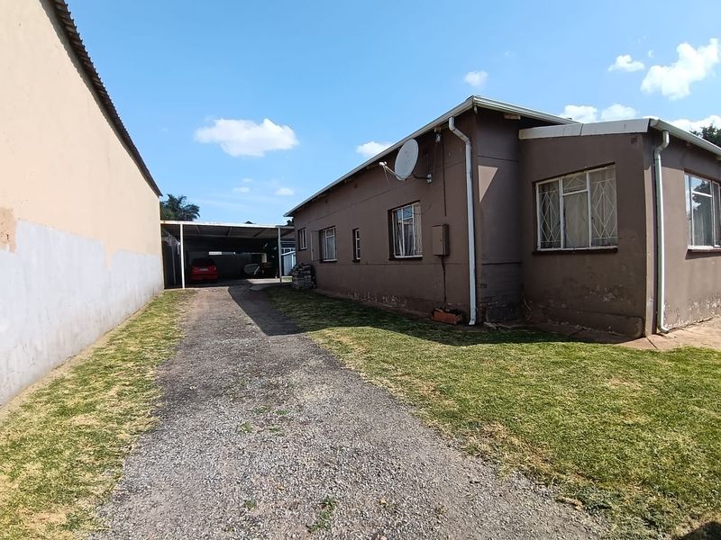 Rear view of the property featuring a gravel driveway, carport, and exterior wall with security bars on the windows.