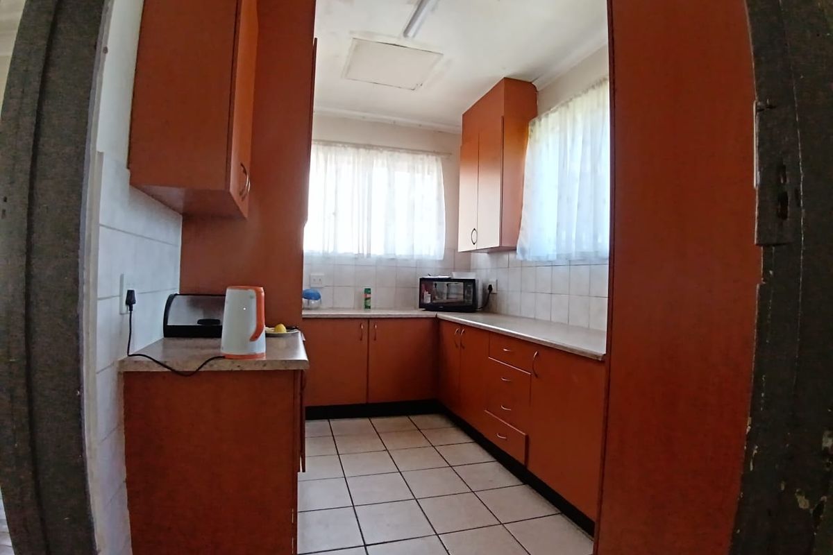 A dated kitchen featuring laminate cabinetry, tiled splashbacks, and ceramic floor tiles, offering a functional layout ready for modernization.