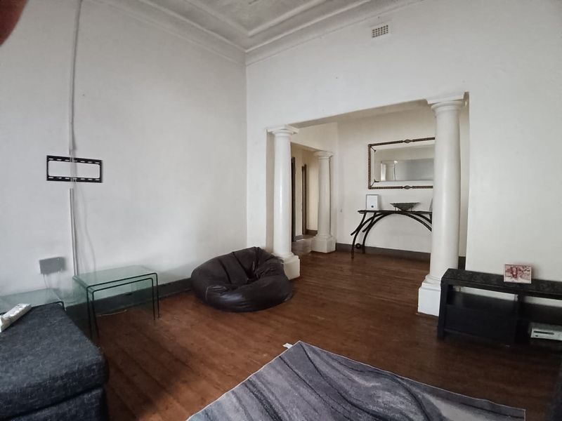 Spacious living area featuring original hardwood flooring, decorative ceiling cornices, and classical columns separating the space.