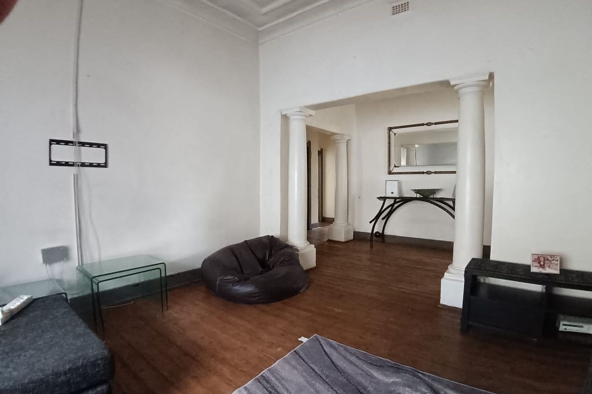 Spacious living area featuring original hardwood flooring, decorative ceiling cornices, and classical columns separating the space.