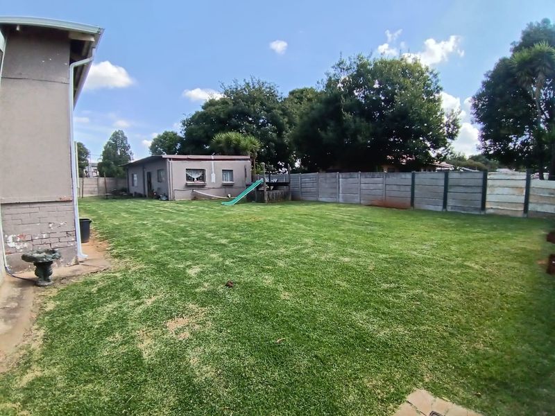 Spacious rear garden featuring a large lawn, precast concrete boundary walling, and a detached outbuilding structure.