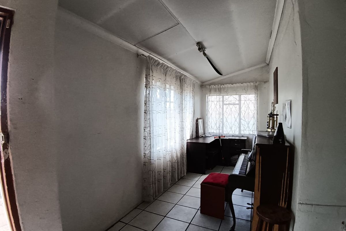 A small bedroom featuring tiled flooring and security bars on the windows, currently used as a multi-purpose space.